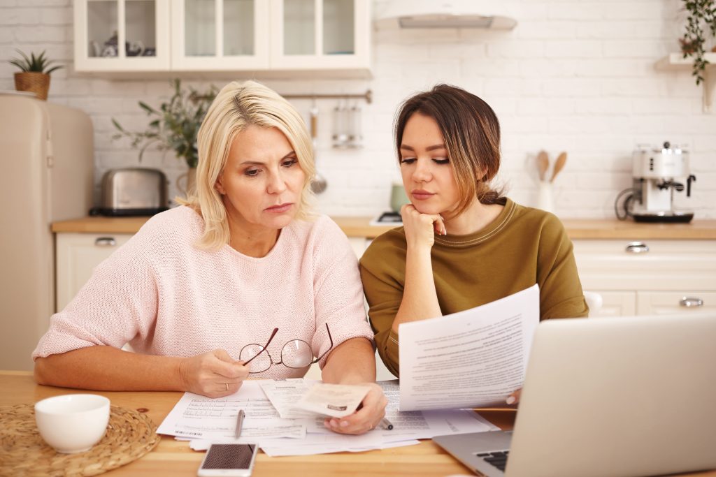 picture of friendly caring young dark haired woman helping mother to fill in financial papers at home. attractive blonde middle aged female is taught to pay utility bills online using laptop picture of friendly caring young dark haired woman helping mother to fill in financial papers at home. attractive blonde middle aged female is taught to pay utility bills online using laptop